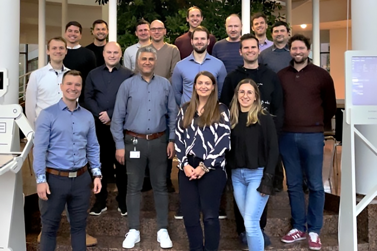 Smiling group with mainly men and two women in the foreground.