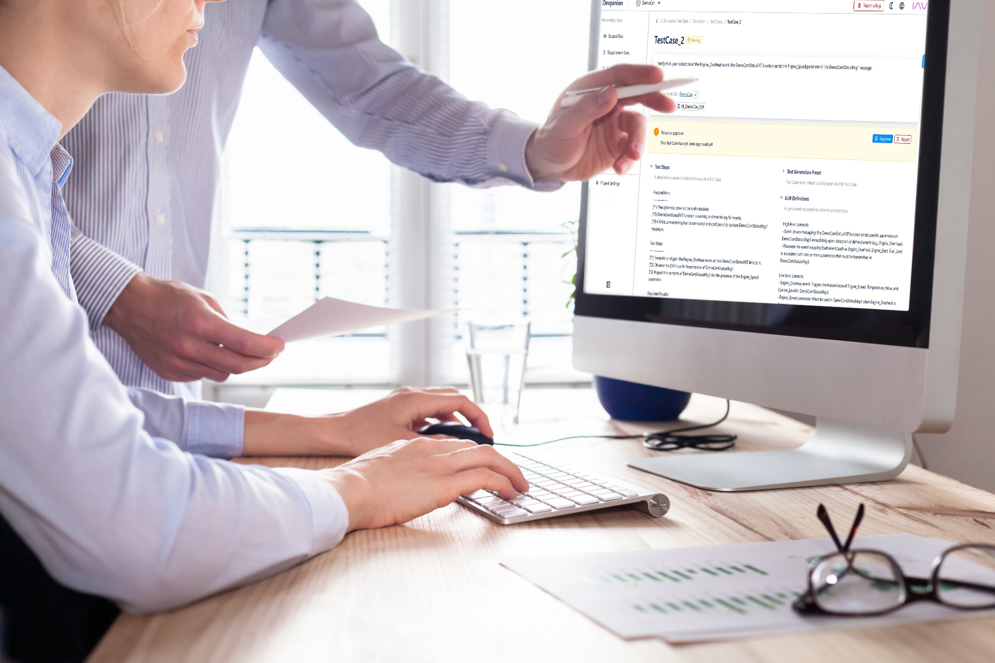 Zwei Personen arbeiten gemeinsam an einem Desktop-Computer im Büro, eine zeigt auf den Bildschirm.