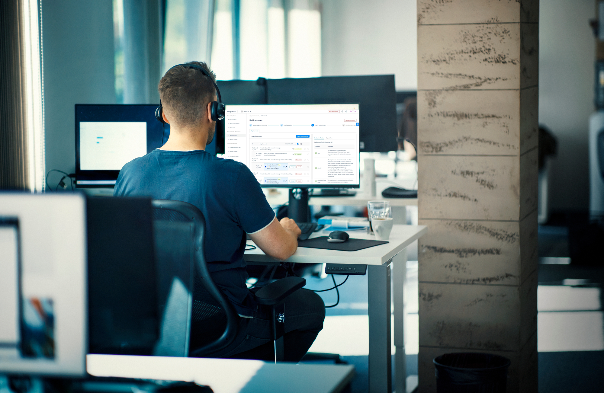 Rückansicht eines Mannes mit Kopfhörern, der vor einem Computerbildschirm in einem Büro sitzt.