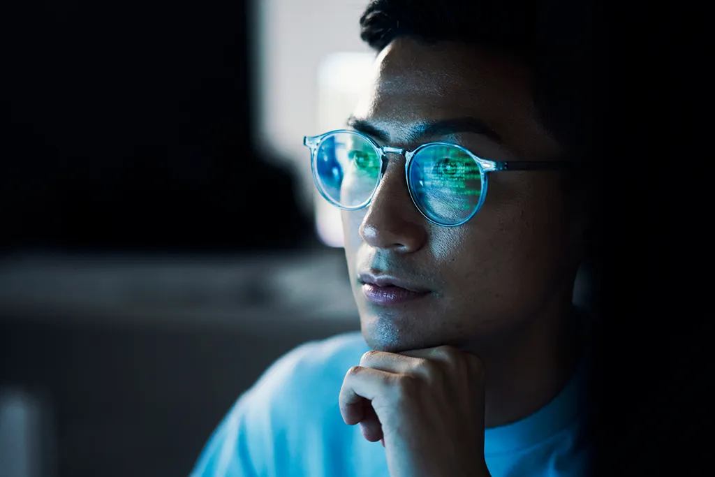 Man looks focused. Code is reflected in his glasses.